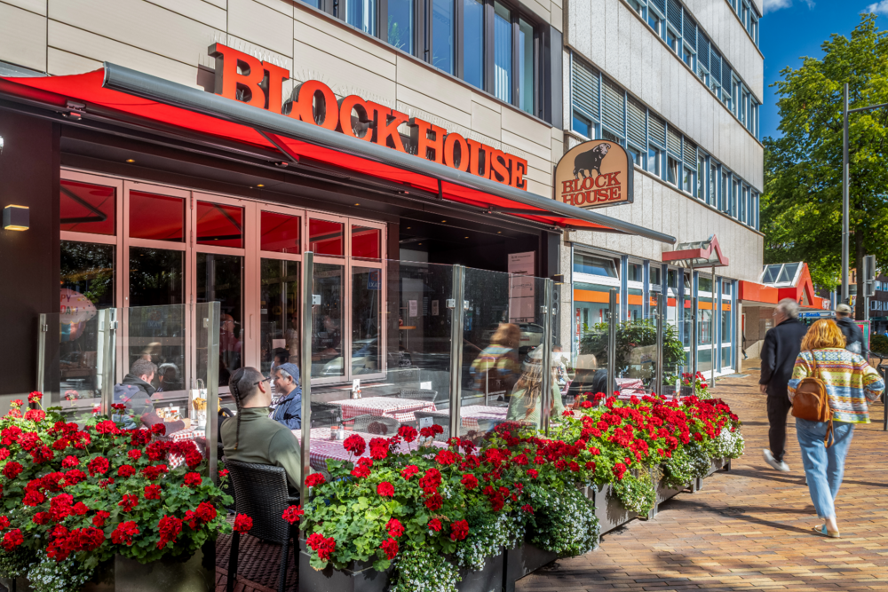 Terrasse des BLOCK HOUSE Hamburg Harburg mit Gästen und rotem Logo auf der Gebäudefassade