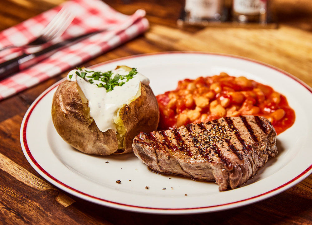 Steak, Ofenkartoffel und Gemüsebeilage liegen auf einem Teller in einem BLOCK HOUSE.