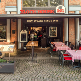 Terrasse des BLOCK HOUSE Ahrensburg mit Gästen an Tischen mit rot-weiß karierten Tischdecken vor dem Steakhouse