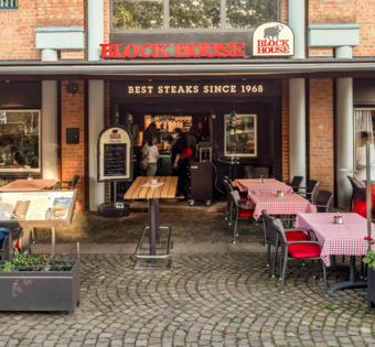 Terrasse des BLOCK HOUSE Ahrensburg mit Gästen an Tischen mit rot-weiß karierten Tischdecken vor dem Steakhouse