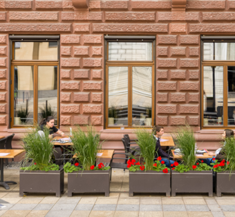 Außenansicht des BLOCK HOUSE Frankfurt am Börsenplatz mit Terrasse, begrüntem Außenbereich und Gästen vor dem Restaurant.