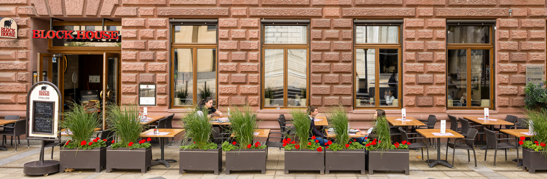 BLOCK HOUSE Frankfurt am Börsenplatz Außenansicht des BLOCK HOUSE Frankfurt am Börsenplatz mit Terrasse, begrüntem Außenbereich und Gästen vor dem Restaurant.