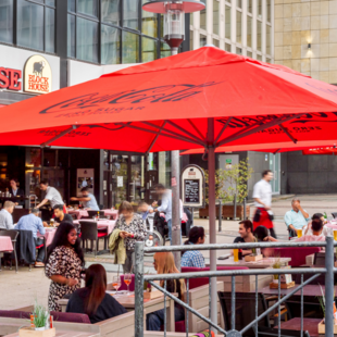 Außenansicht des BLOCK HOUSE Essen mit großer Terrasse, roten Sonnenschirmen und Gästen im Außenbereich.
