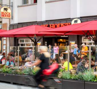 Terrasse des BLOCK HOUSE Hannover Am Kröpcke mit Gästen unter roten Sonnenschirmen in der Fußgängerzone der Innenstadt