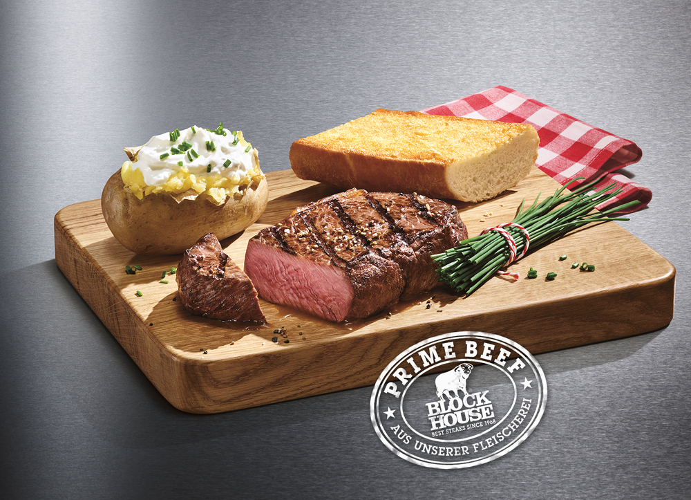 Ein gegrilltes, zartrosa Rumpsteak vom BLOCK HOUSE Rind, serviert auf einem Holzbrett mit einer original Baked Potato und ofenfrischem Block House Brot.