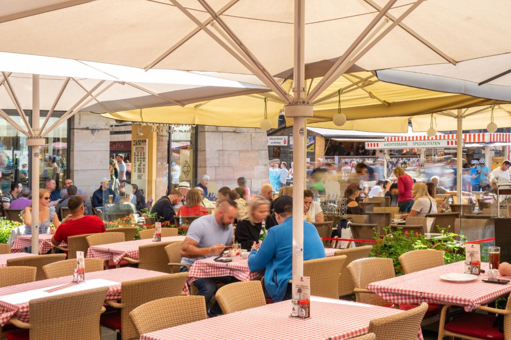 Gäste speisen zur Mittagszeit auf der sonnengeschützten Außenterrasse des BLOCK HOUSE Nürnberg am Hauptmarkt in der Altstadt