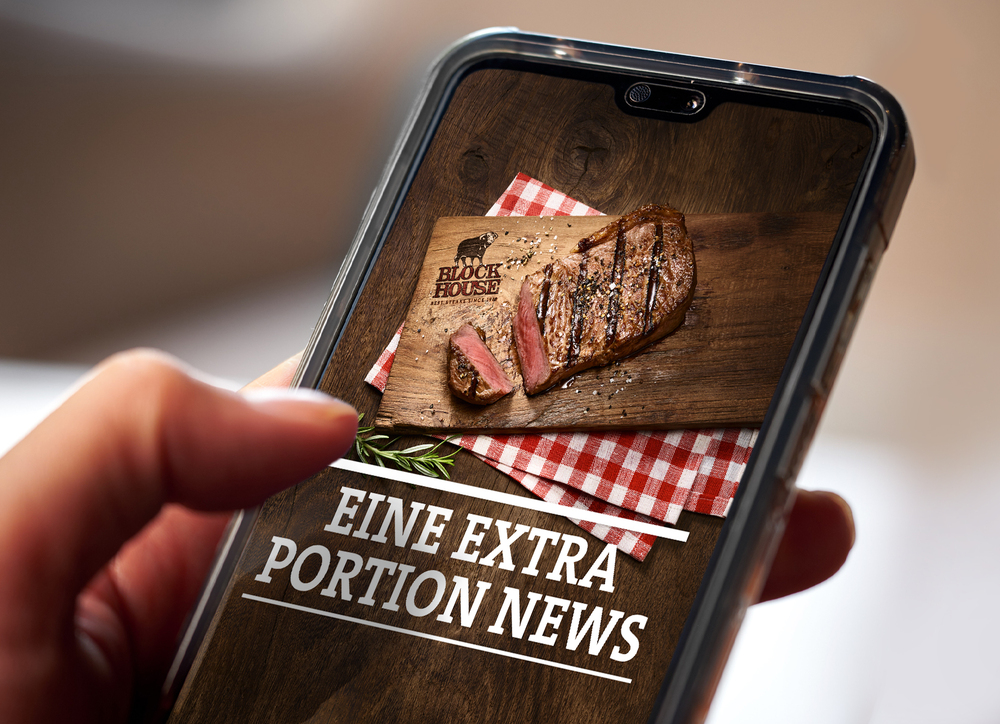 Person hält Handy in der Hand, wo ein Teaser des BLOCK HOUSE Website Newsletters mit der Aufschrift "Eine extra Portion News" mit einem Steak zu sehen ist